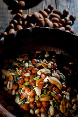Many types of nuts close up. Texture of different nuts on a wooden board. Clay bowl on a brown table. Contrasting dramatic light as an artistic effect.
