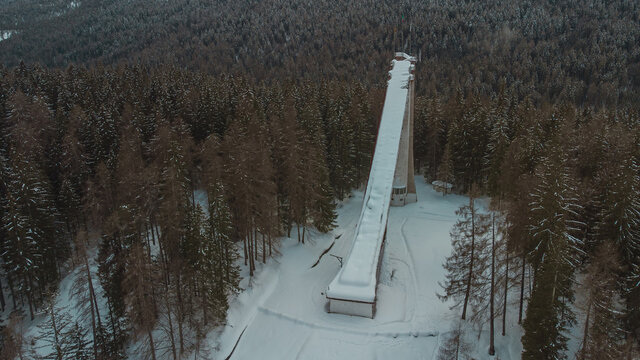 Aerial drone view of old deserted or abandoned famous ski jumping hill in Cortina d'Ampezzo, Italy on a winter day with snow.  Visible snowy forest in the background.