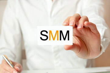 A woman in a white shirt holds a piece of paper with the text: SMM. SMM - Social media marketing. Business concept.