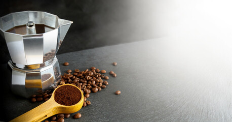 Ground coffee and moka pot with coffee beans around on the dark blur background. 
