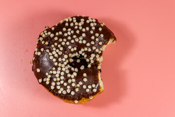 Bitten tasty chocolate donut on a pink background. Top view