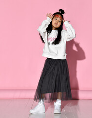 Portrait of a stylish Korean girl wearing a white sweater, tulle skirt, sneakers and red...