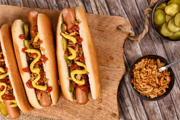 Homemade hotdogs with sausages and buns topped with preserved pickles, dried roast onions, mustard...