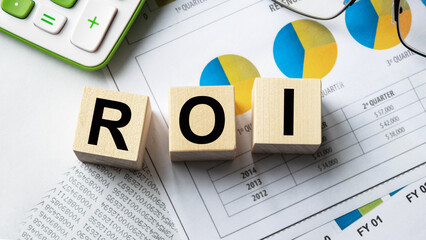 The inscription on the cubes, the word ROI on the cubes of wooden texture. View from above. Desktop with documents. An inscription on a financial, business or economic theme.