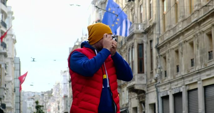 tourist in a red vest walks around Salzburg and takes a photo with a film camera