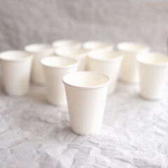 disposable cups made of white paper are laid out on gray crumpled paper