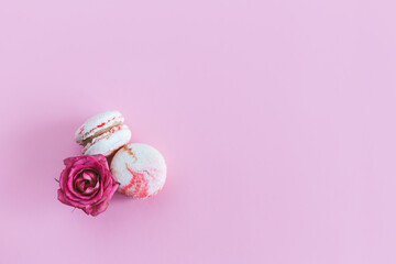 Tasty french macaroons with pink roses on a pink pastel background.
