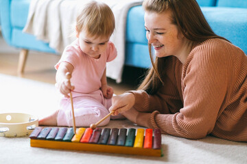 Mother and one and a half year old girl play musical instruments: xylophone, harmonica, tambourine....