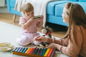 Mother and one and a half year old girl play musical instruments: xylophone, harmonica, tambourine....
