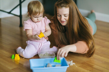 A young mother and her one and a half year old daughter are sculpted from kinetic sand. Development of motor skills