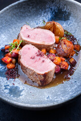Modern style traditional roasted dry aged veal tenderloin with jus and braised winter root vegetable served as close-up in a design bowl