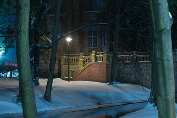 Park Dworski w Iłowej w zimową noc. Kamienny mostek nad rzeką.