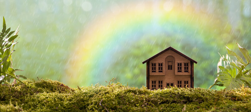 Eco-friendly house. Wooden house on forest moss. Background is rainbow. World environmental awareness concept