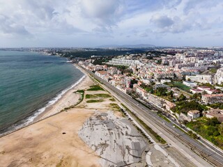 Aerial view of Lisbon south coastline along the Tagus river with a residential district on the hilltop, view of a straight road driving along the coast, Portugal.
