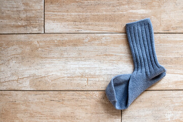 A single ribbed mid-calf blue wool sock that is missing its partner lies on a gold-beige tile floor...