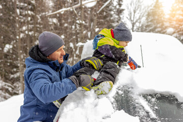 Fototapeta na wymiar Shoto of a mature men and his cute little child removing snow from car after blizzard. Young man with his adorable little son having a fun while cleaning car from snow at the backyard of the house.