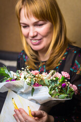 A woman admires a gorgeous bouquet. The blonde looks at a beautiful flower arrangement. Congratulations on Women's Day, Mother's Day, Birthday. Vertical photography. Selective focus