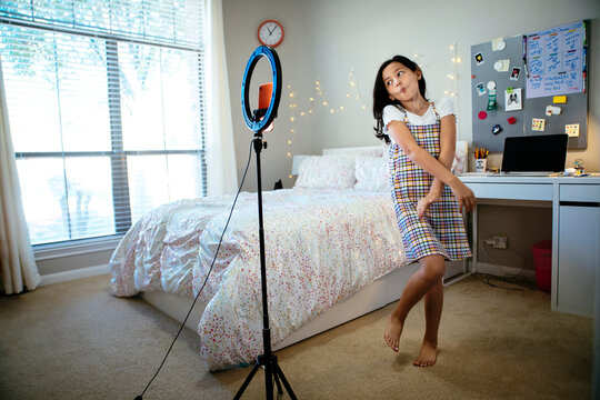 Happy tween girl making dancing video for tiktok social media on cell phone in bedroom