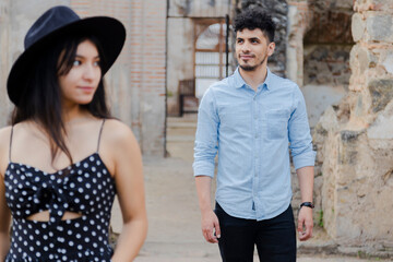 Creative portrait of Hispanic couple among famous ruins of Antigua Guatemala-Hispanic young man smiling looking at the horizon with his girlfriend in front out of focus - distanced couple