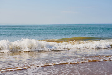 Waves with foam on the sandy beach of the Mediterranean Sea going beyond the horizon.