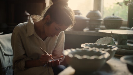 Beautiful woman making ornament on product in pottery. Girl drawing on wet clay