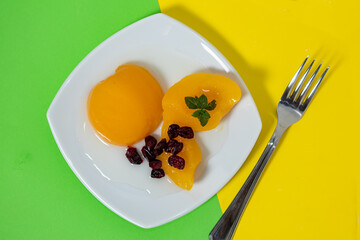 delicious peaches in syrup in a glass bowl on a colored surface and some cranberries.