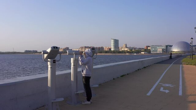 A young girl examines the skyscrapers on the coast with binoculars for the observation deck on the embankment. View from the Lakhta center embankment