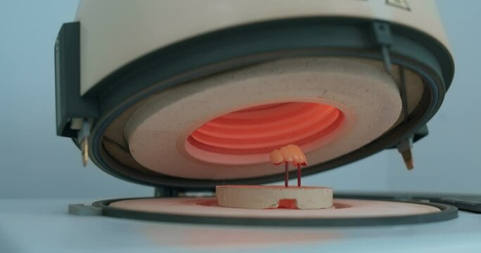 A model of teeth prothesis is standing inside a huge dental ceramic furnace. 
There is orange light inside the dental technician device.