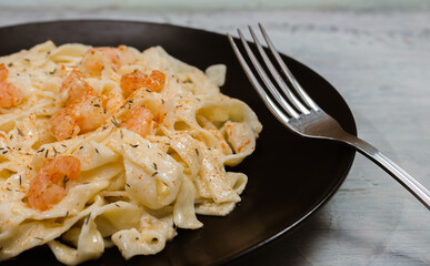 Delicious Italian pasta. Fetuccini with shrimp and herb sauce on black plate and light background.