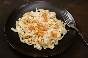 Delicious Italian pasta. Fetuccini with shrimp and herb sauce on black plate and dark background.