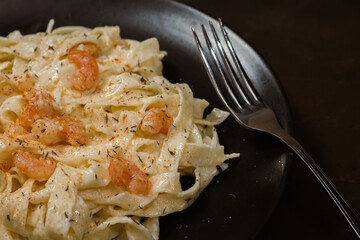 Delicious Italian pasta. Fetuccini with shrimp and herb sauce on black plate and dark background.