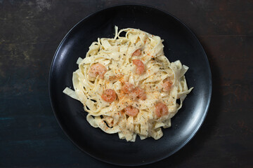 Delicious Italian pasta. Fetuccini with shrimp and herb sauce on black plate and dark background.