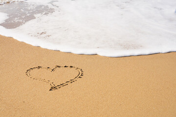 Heart painted on the sand on the beach and foam from the waves.