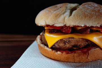 Delicious hamburger with Bacon and cheddar cheese on homemade bread with seeds and ketchup on a wooden surface and Black background.