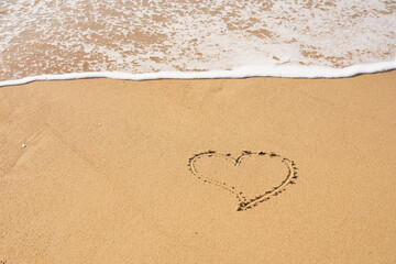 Heart painted on the sand on the beach and foam from the waves.