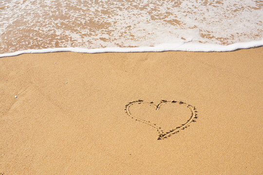 Heart painted on the sand on the beach and foam from the waves.