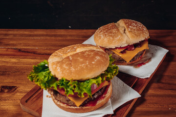 Delicious burgers with Bacon and cheddar cheese and with lettuce, tomato and red onion and bacon and cheddar on homemade bread with seeds and ketchup on a wooden surface and black background.