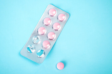 Pink medical pills and tablets isolated on blue background. Photography top view with copy space. Medical concept.