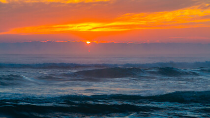 Sunrise at sea. The sun rises over the horizon of the sea and a new day begins. Panoramic sea landscape on sunset or sunrise with ocean waves and orange colorful clouds in sky.