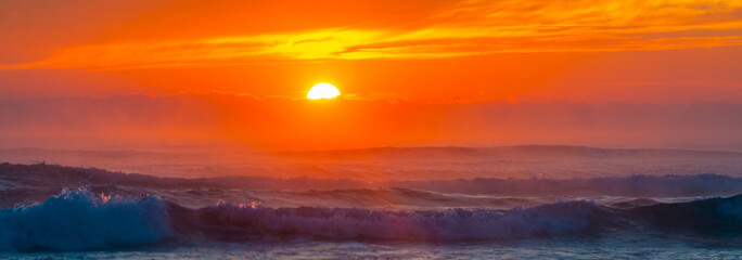 Sunrise at sea. The sun rises over the horizon of the sea and a new day begins. Panoramic sea landscape on sunset or sunrise with ocean waves and orange colorful clouds in sky.