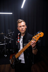 Obraz premium brutal portrait of a man musician in black clothes against the background of musical instruments holding a guitar in his hands