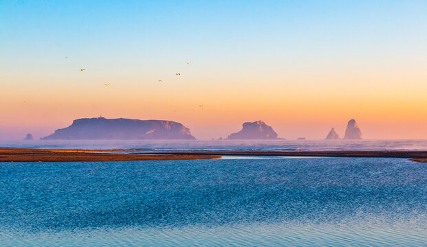 Mouth of the river Ter in the Mediterranean Sea with the Medes Islands and Estartit in the background. Panoramic sunrise landscape with the river flowing calmly. Morning lights with calm atmosphere.