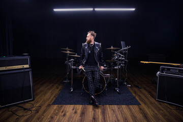 brutal portrait of a man musician with a beard and in black clothes on the background of musical instruments drums
