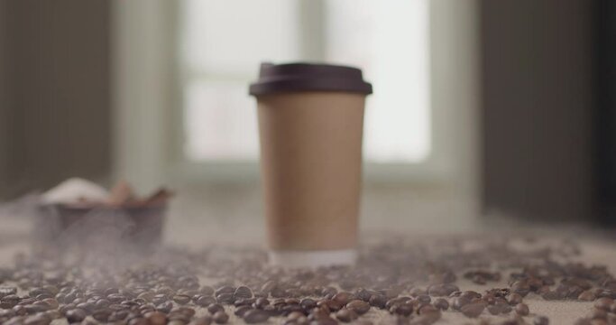 A glass with a drink of coffee. A takeaway paper cup in a cafe stands on a table with coffee beans in the kitchen with latte, cappuccino or espresso. Background 4K slow motion video.