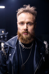 brutal portrait of a man musician with a beard and in black clothes on the background of musical instruments drums