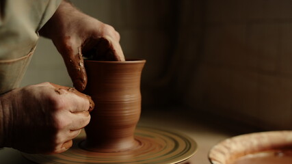 Fototapeta na wymiar Unknown clay artist sculpting in studio. Man hands forming jar in pottery 
