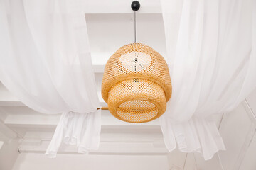 stylish wicker wooden chandelier in boho and Bali style hangs on the ceiling near a white canopy...