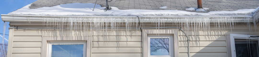 gutters have frozen and icicles hang from the ice dams panorama