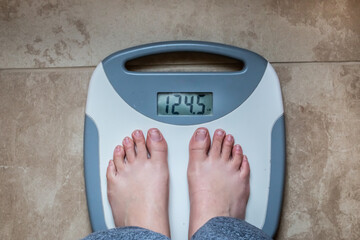 A woman with bare feet wearing sweatpants in her bathroom on a gray and white scale set against...