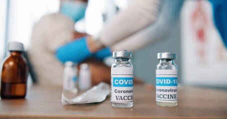 Close up shot of coronavirus vaccine ampoules with liquid, ampoule with vaccine from covid-19 on table in clinic room, doctor making injection on background, injection set, vaccination concept